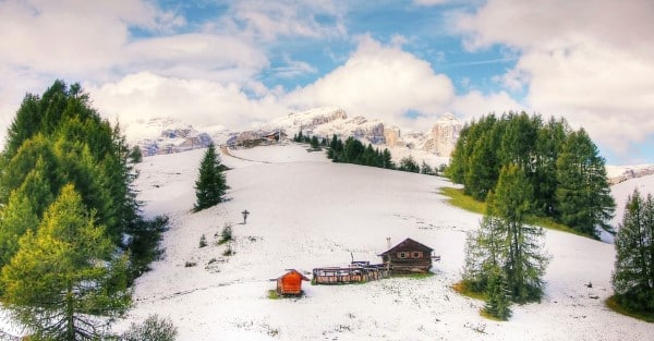 Mariaalm mit leicht verschneiter Landschaft, ein Hügel mit einer Alm und grünen Bäumen im Schnee
